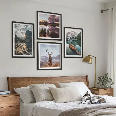 Billedvæg over sofa med motiv af bjerge, sø, båd, solnedgang og hjorte