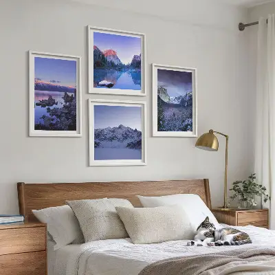 Billedvæg over sofa med bjerglandskaber, solnedgang og vand